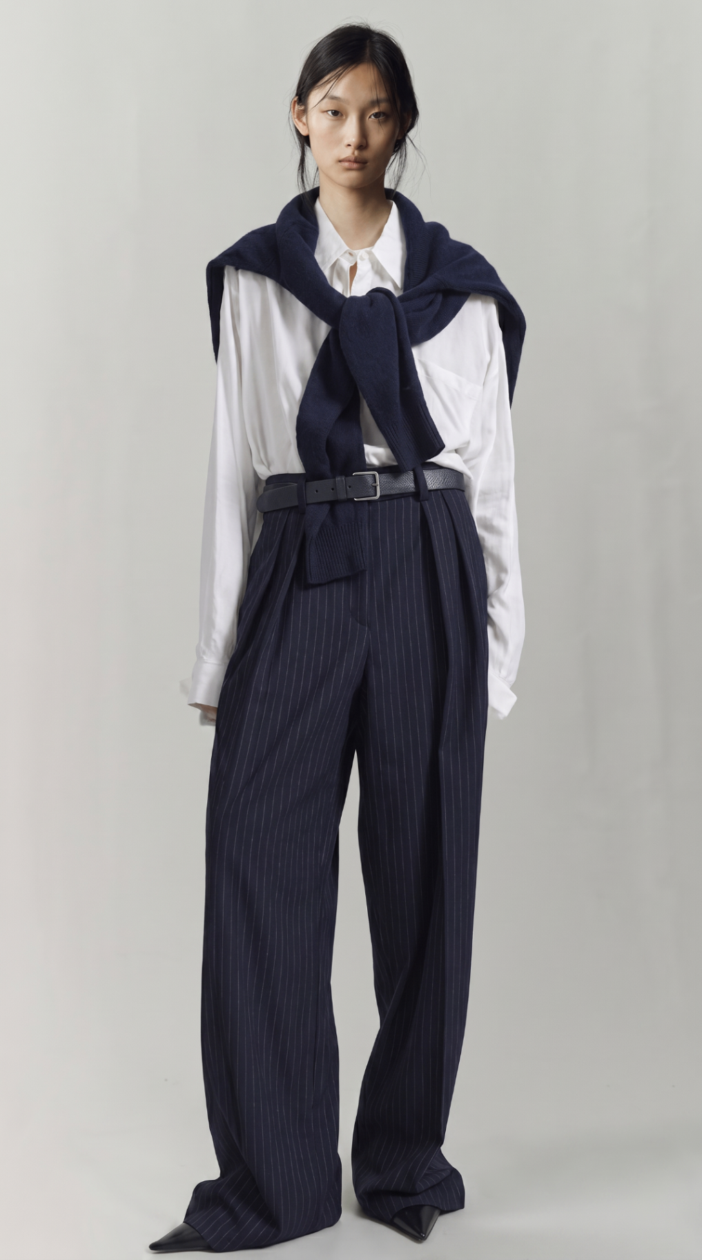 Look 08 — white shirt with a navy knit draped over the shoulders and fluid pinstriped trousers cinched with a black belt.
