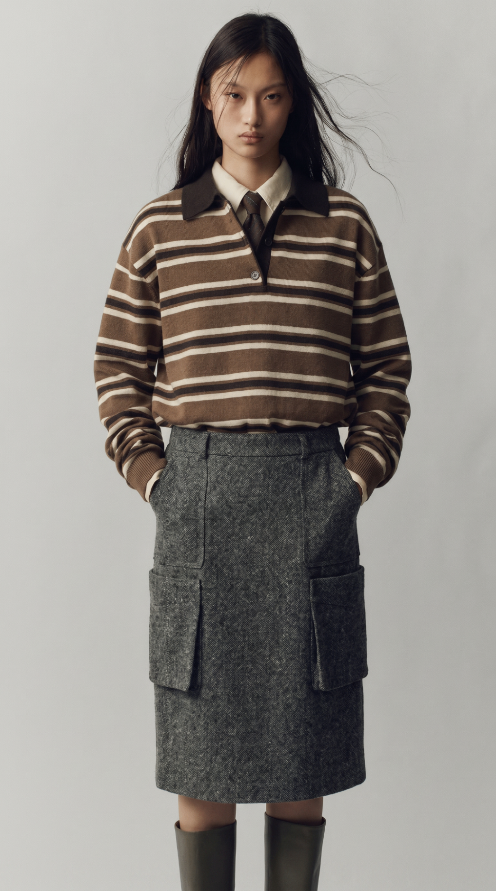 Look 10 — brown striped rugby knit layered over shirting and a tie with a grey pocket skirt and tall boots.