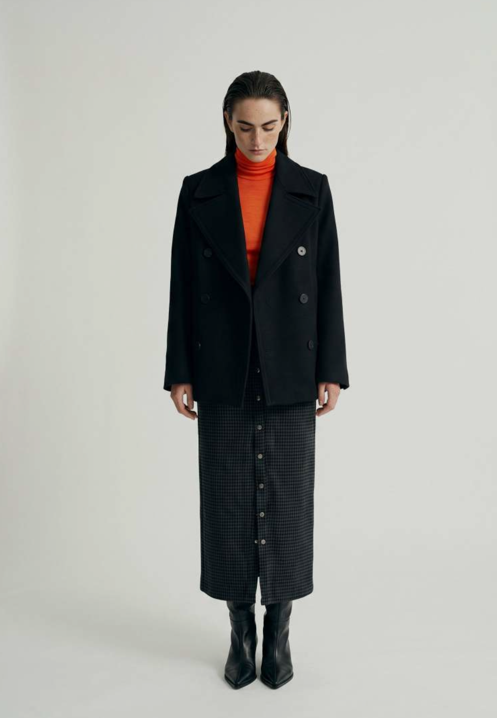 Navy double-breasted peacoat over an orange turtleneck with a checked button-front midi skirt and black boots.