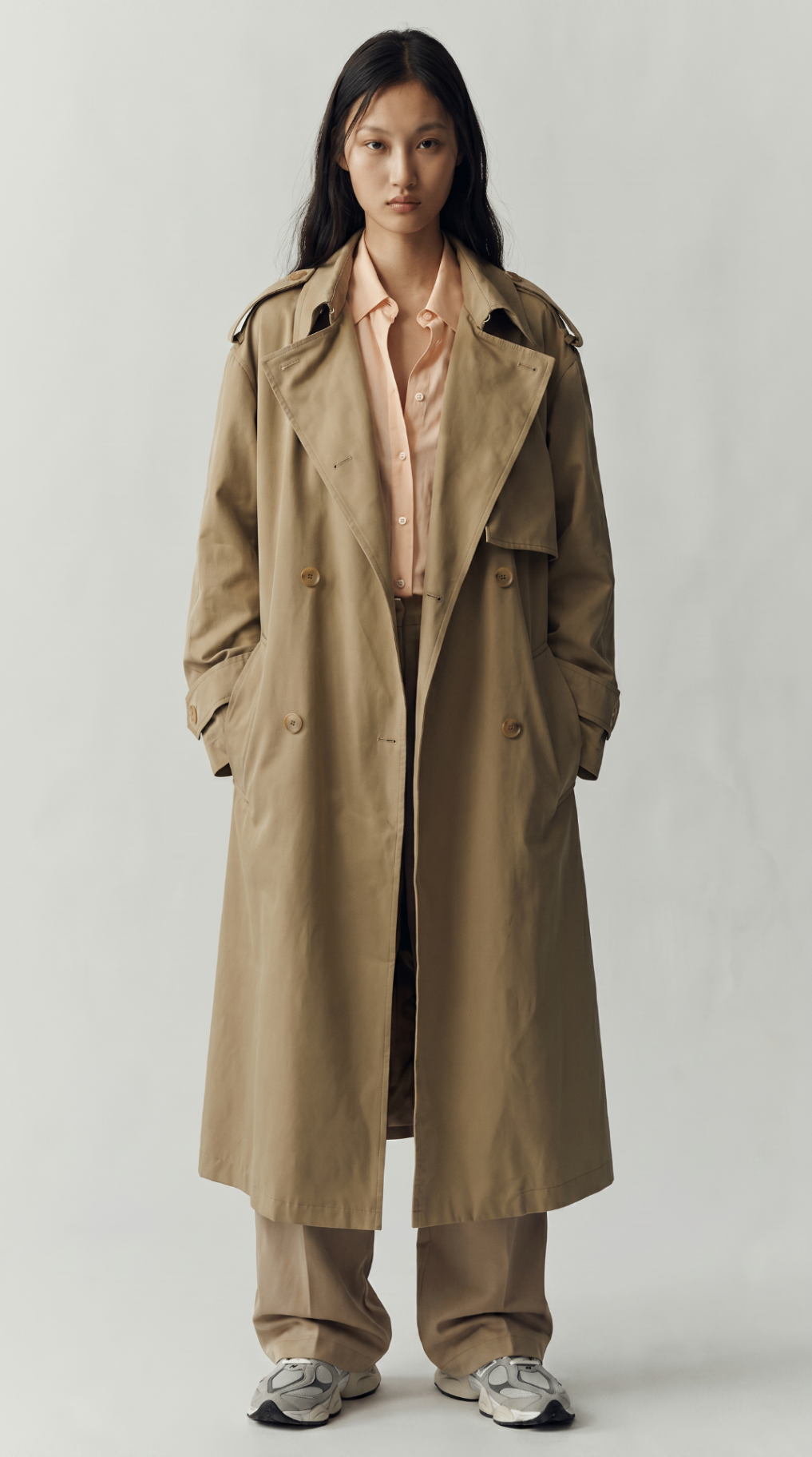Look 07 — long sand trench over a blush shirt with tonal tailoring and silver trainers.