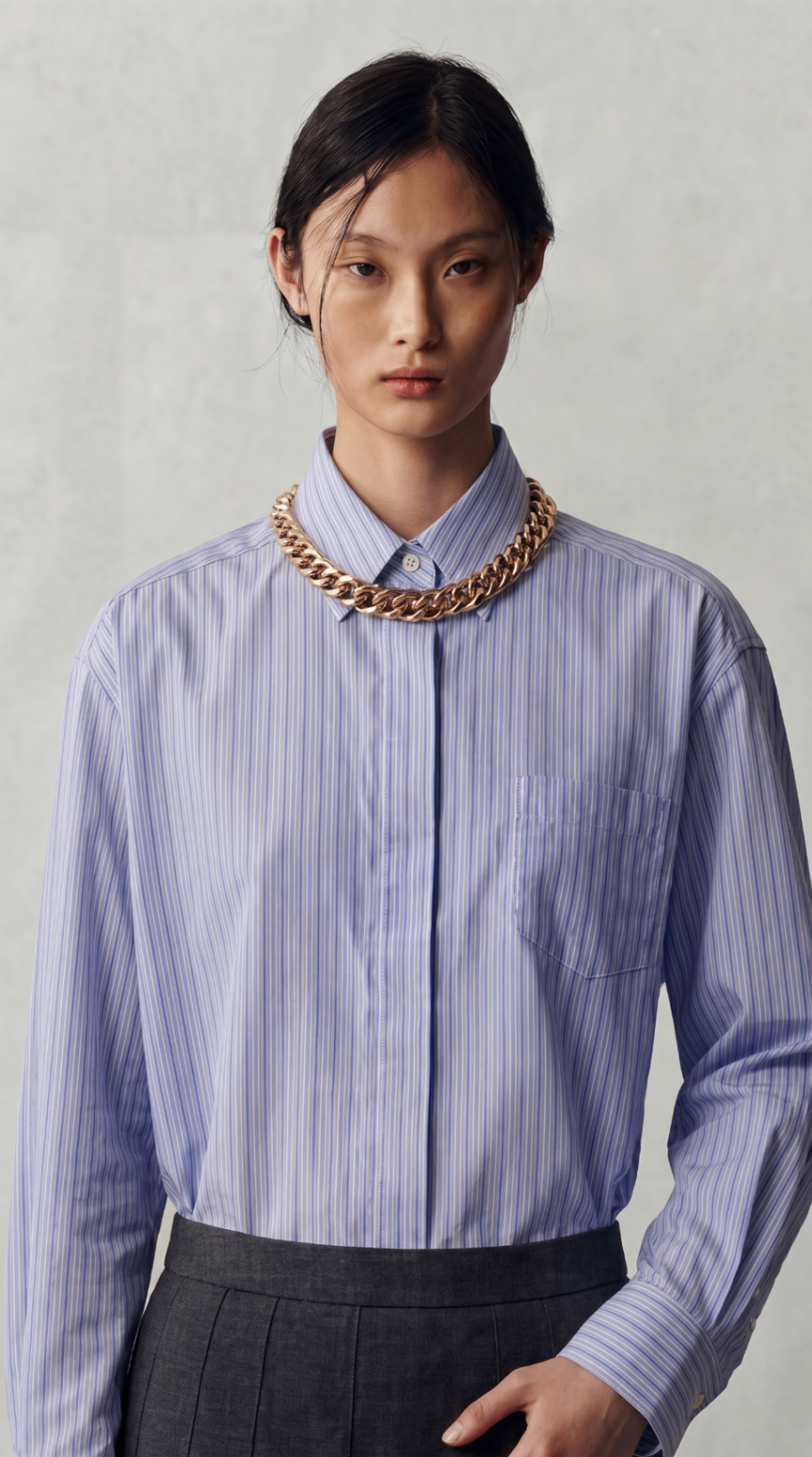 Look 12 — blue striped shirt finished with an oversized gold chain and dark pleated skirt.