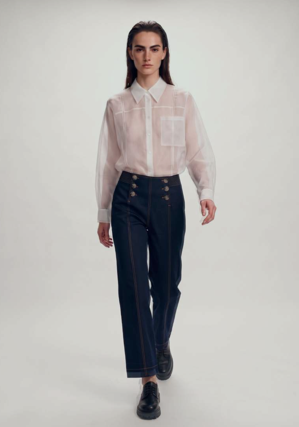 Sheer white organza shirt with high-waisted navy sailor-button denim trousers.
